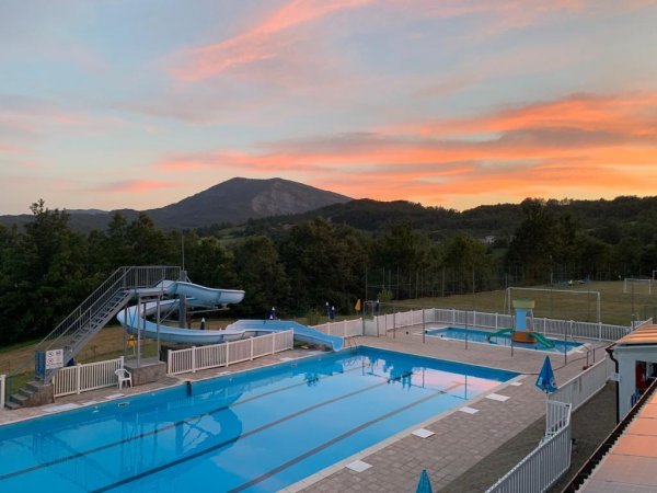 Piscina all'aperto con scivolo e tramonto sullo sfondo.