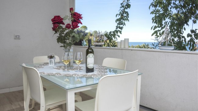 Tavolo con bicchieri di vino e rose rosse, affacciato su una vista mare.