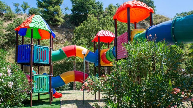 Un colorato parco giochi con scivoli e altalene tra alberi e cespugli.