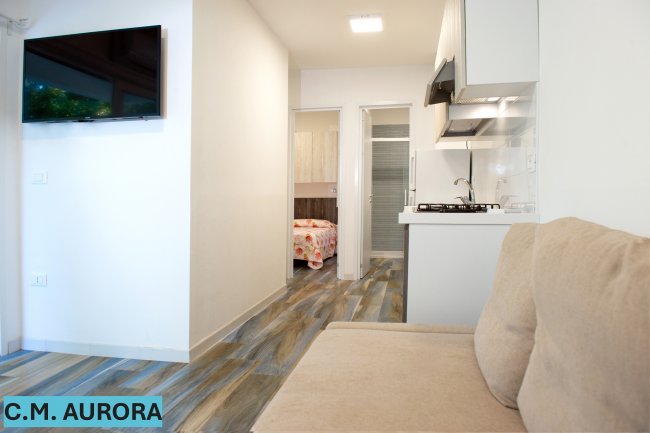 Interno moderno con divano, TV a muro e cucina accogliente.