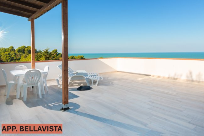Terrazza con tavolo, sedie e sdraio, vista panoramica sul mare.
