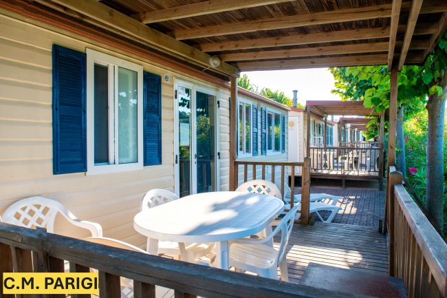 Veranda in legno con tavolo bianco e sedie, affacciata su giardino.