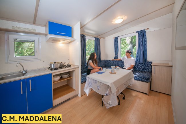 Interno di una casa mobile con angolo cottura blu e due persone sedute a un tavolo.
