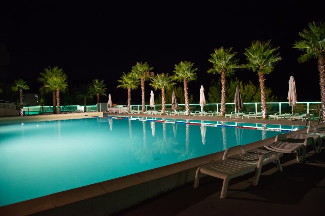 Una piscina illuminata di notte, circondata da lettini e palme.