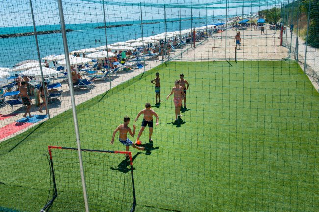 Gruppo di ragazzi gioca a calcio su un campo vicino alla spiaggia.