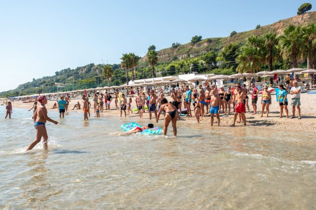 Turisti su una spiaggia affollata, alcuni in acqua, altri a riva.