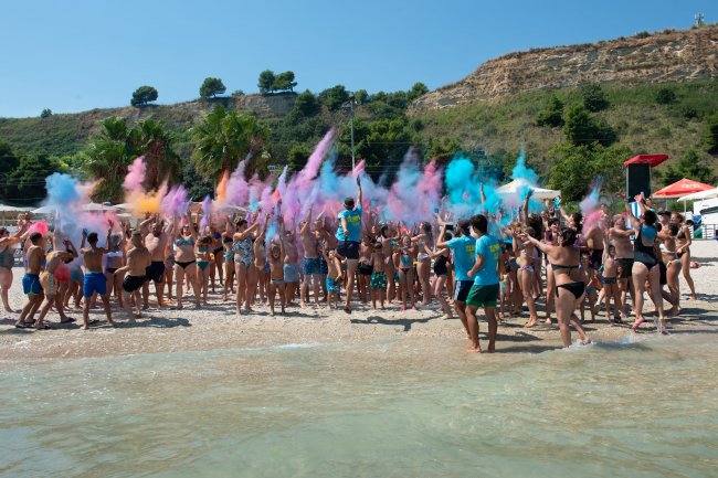 Festa in spiaggia con polveri colorate lanciate in aria.