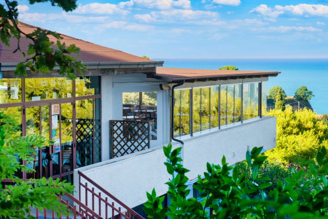 Edificio bianco con ampie finestre vicino al mare sotto un cielo azzurro.