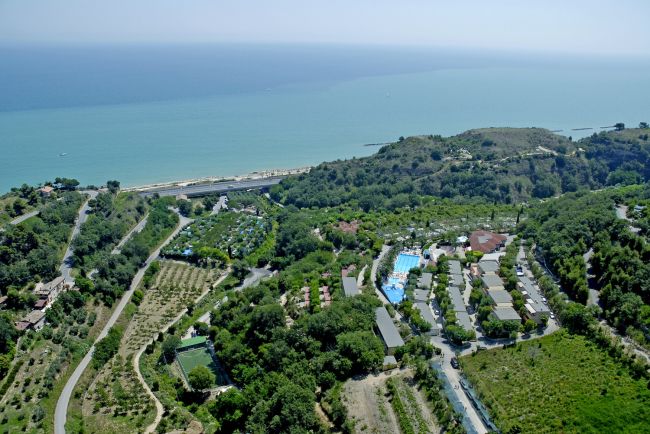 Vista aerea di un campeggio vicino alla costa, circondato da verde e colline.