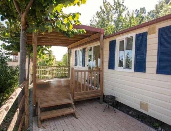 Esterno di una casa mobile con veranda in legno e finestre blu.