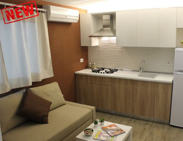 Cucina moderna con divano, armadietti bianchi, fornelli e frigorifero.