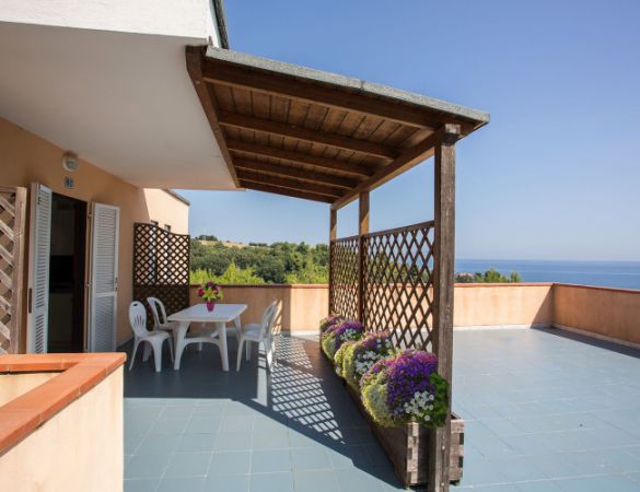 Terrazza con tavolino, sedie, fioriere e vista mare.