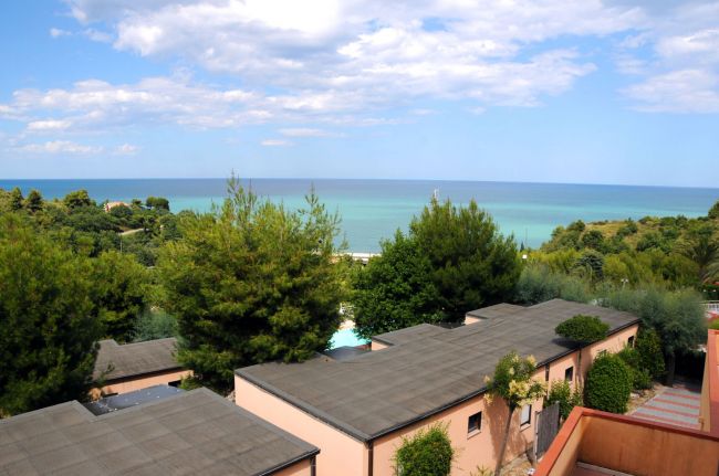 Panorama con tetti di edifici, alberi e mare all'orizzonte.
