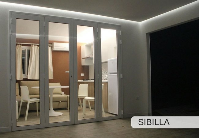 Porta a vetri che dà su un soggiorno con cucina, tavolo e sedie bianche.