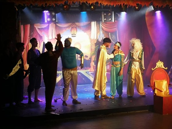 Una scena teatrale con attori in costumi colorati su un palco illuminato.