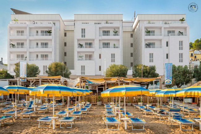 Spiaggia con ombrelloni gialli e blu, e un edificio bianco sullo sfondo.