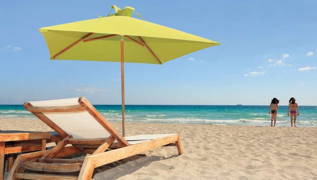Lettino e ombrellone su una spiaggia con due persone vicino al mare.