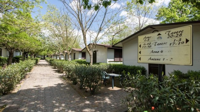 Vialetto tra bungalow e siepi, con un cartello di indicazioni.