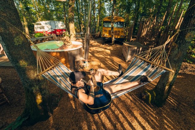 Persona su un'amaca con chitarra in un bosco.