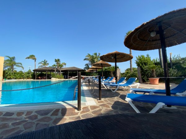 Piscina con lettini blu e ombrelloni di paglia.