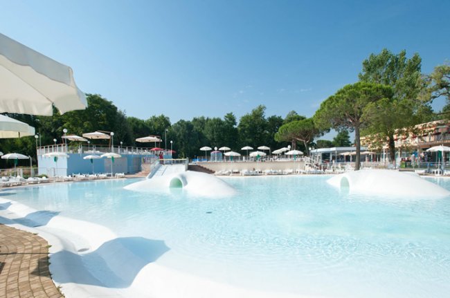 Grande piscina all'aperto con ombrelloni e alberi.