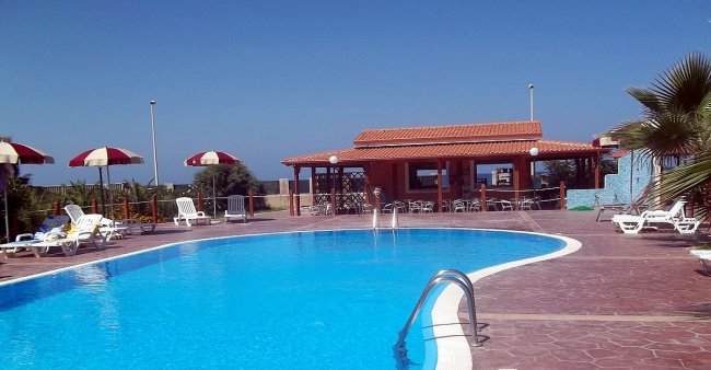 Piscina con ombrelloni e un edificio sullo sfondo.