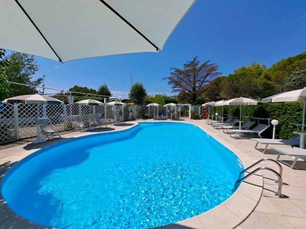 Piscina con sdraio e ombrelloni sotto un cielo sereno.