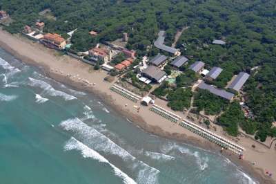 Vista aerea di una spiaggia e mare con edifici e vegetazione sullo sfondo.