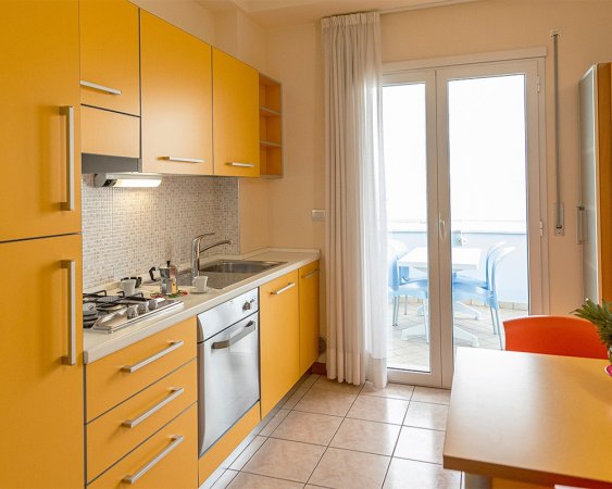 Cucina con mobili gialli e accesso al balcone.