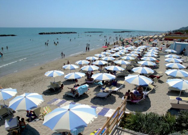 Spiaggia affollata con ombrelloni bianchi e blu.