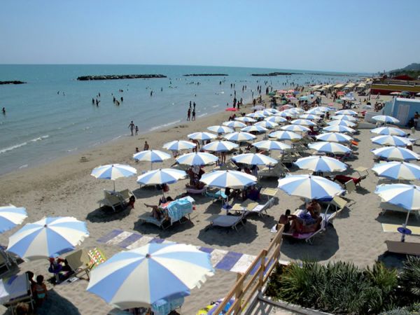 Spiaggia con ombrelloni bianchi e blu, e persone che si godono il sole e il mare.