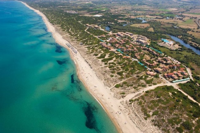 Costa sabbiosa con mare azzurro e vegetazione.