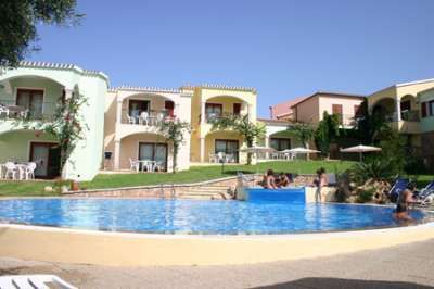 Piscina all'aperto con persone, circondata da edifici colorati con terrazze.
