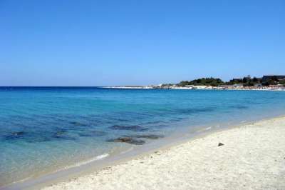 Spiaggia con sabbia bianca e mare turchese sotto un cielo azzurro.
