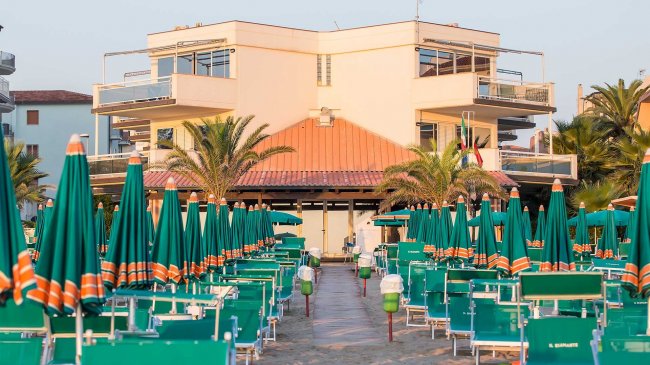 Percorso tra ombrelloni verdi verso edificio.