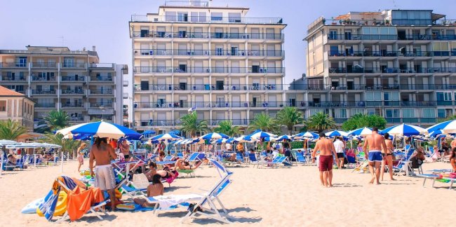 Spiaggia affollata con ombrelloni davanti a palazzi.