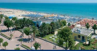 Spiaggia attrezzata con ombrelloni vicino a una passeggiata con palme e strutture.