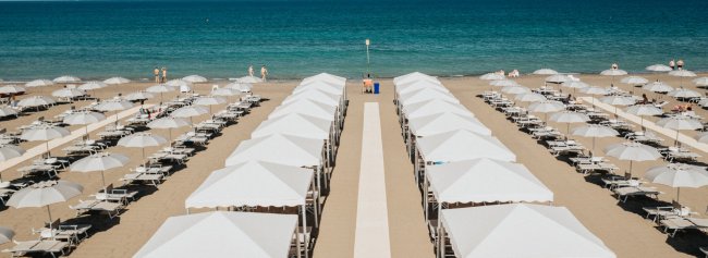 File ordinate di ombrelloni bianchi su una spiaggia sabbiosa.