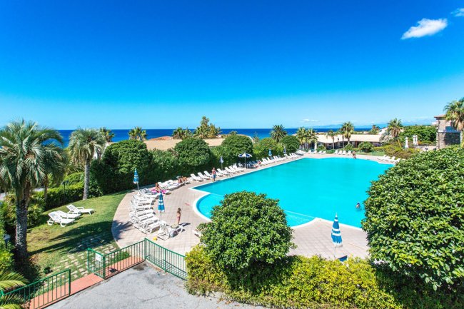 Una grande piscina all'aperto circondata da sdraio, ombrelloni e vegetazione rigogliosa.