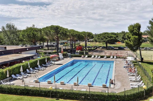 Piscina rettangolare con sdraio e ombrelloni bianchi.