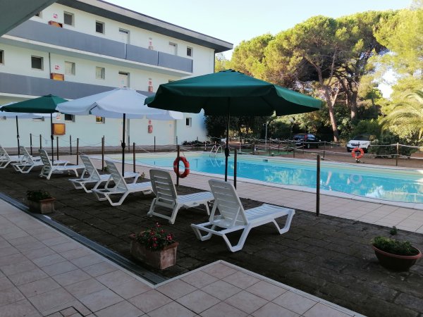 Piscina con lettini bianchi e ombrelloni verdi.