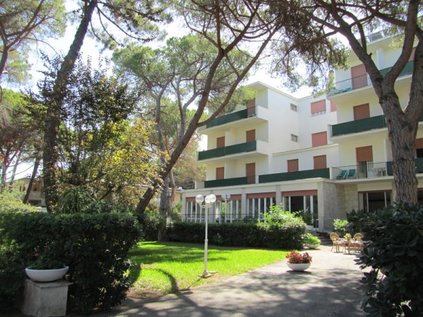 Edificio bianco, giardino con alberi e vialetto con prato.