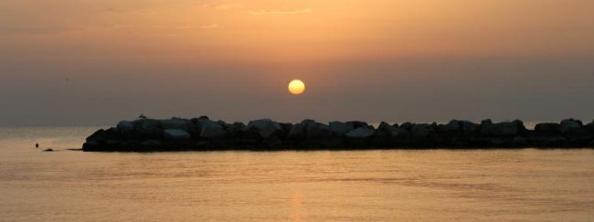 Tramonto su un mare calmo con scogli.