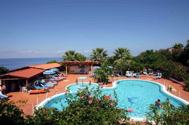 Piscina all'aperto con lettini, ombrelloni e vista mare.