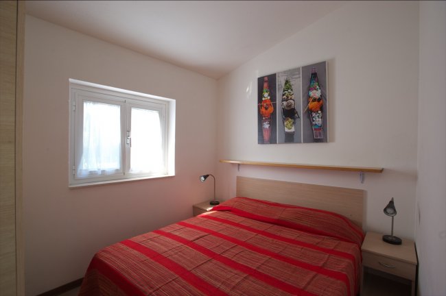 Piccola camera da letto con copriletto rosso e finestra.