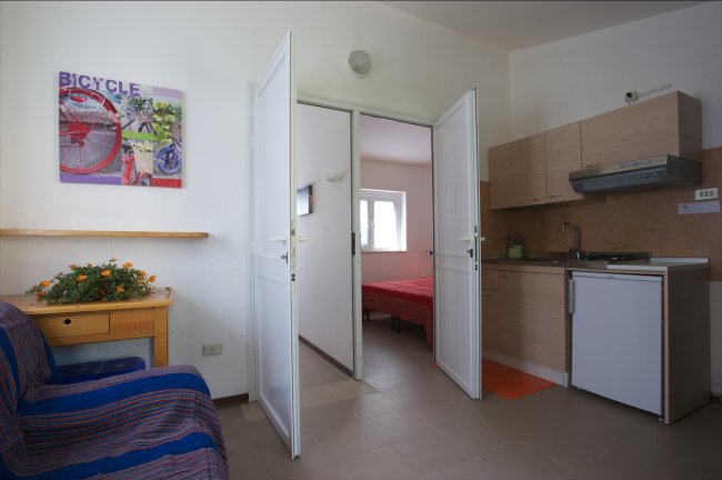 Sala con divano, cucina e vista su camera da letto.