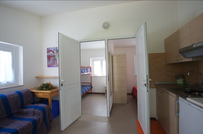 Sala con divano, cucina e vista su due camere.