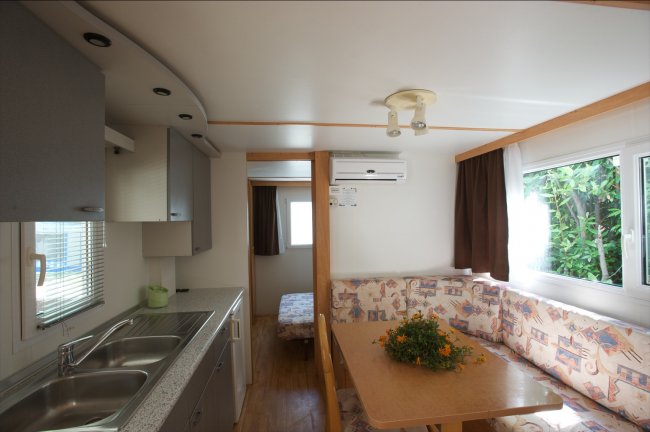 Interno di una casa mobile con cucina, divano angolare e finestre.