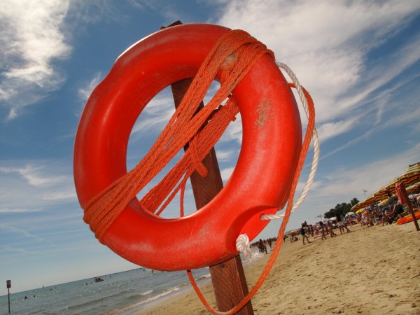 Salvagente rosso sulla spiaggia con ombrelloni.
