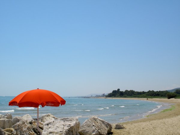 Spiaggia con ombrellone rosso e mare azzurro.